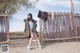 A woman sitting on a wooden fence in the sand.