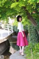 A woman in a pink skirt standing next to a river.