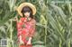 A woman in a red dress and straw hat standing in a corn field.